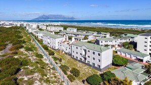 Una zona residencial costera con edificios modernos, vistas al océano y una cadena montañosa distante.
