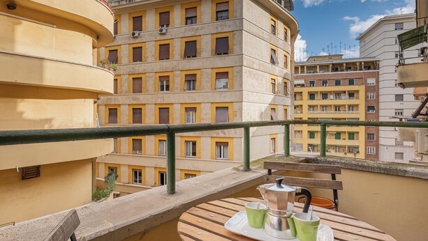 A balcony with a wooden table, a metal coffee pot, and two green cups.