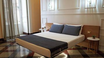 Habitación de hotel con una cama grande, una mesita redonda con una planta y una ventana con cortinas.
