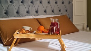 A bed with a grey tufted headboard, a brown pillow, and a wooden tray with croissants, a cup, an orange, and a pitcher of red beverage. - Toscano Palace Luxury Rooms Catania (Catania)