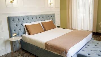 A bedroom with a tufted headboard, a round side table, a bench, and a bed with a beige and brown blanket.
