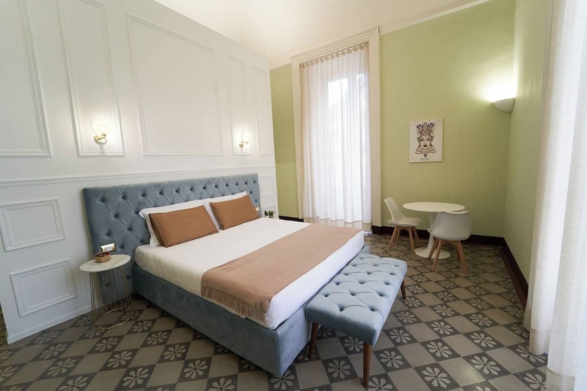 A bedroom with a large bed, a bench, a small table, and a chair.