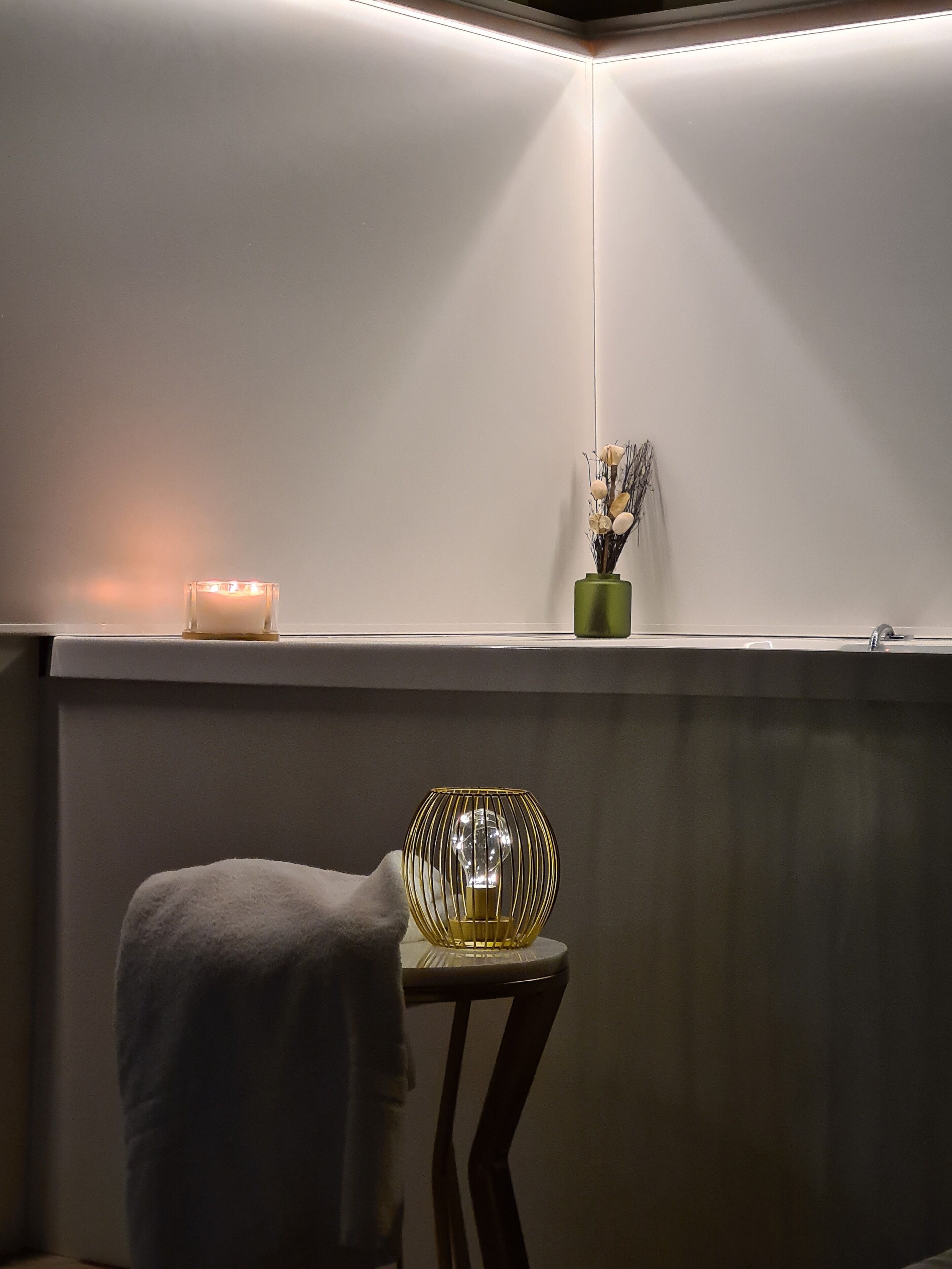 Un rincón de una habitación con una pared blanca, una mesita con un florero de cristal y una vela en la pared.