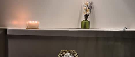 Un rincón de una habitación con una pared blanca, una mesita con un florero de cristal y una vela en la pared.