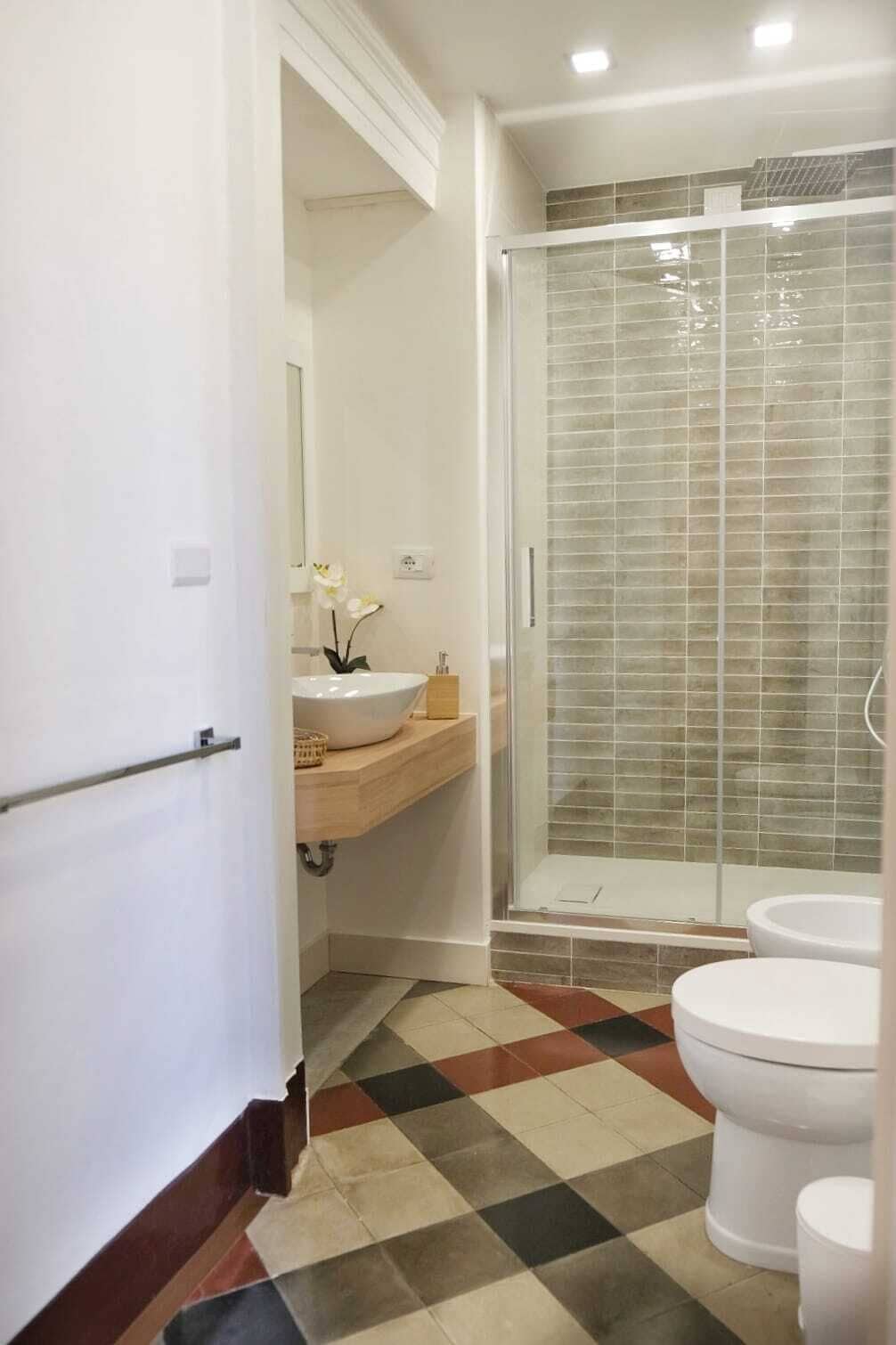 A bathroom with a glass-enclosed shower, a white sink, and a checkered floor pattern.