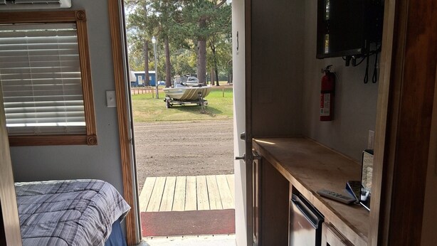 A compact RV interior with a bed, kitchenette, and a door leading to an outdoor area with a boat. - Charming remodeled motel room in Hemphill with Wi-Fi, mini fridge & microwave.   (Hemphill)