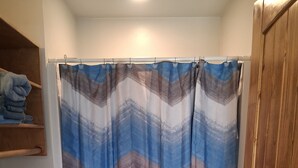 A bathroom with a striped shower curtain, a toilet, and wooden cabinets. - Charming remodeled motel room in Hemphill with Wi-Fi, mini fridge & microwave.   (Hemphill)