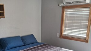 A bedroom with a bed, a window with blinds, and an air conditioning unit on the wall. - Charming remodeled motel room in Hemphill with Wi-Fi, mini fridge & microwave.   (Hemphill)