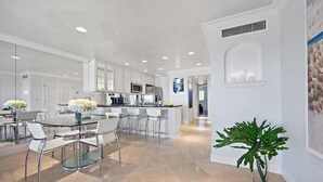 A modern kitchen with white cabinetry, a glass dining table, and a large island. - 604 Surf Villas Oceanfront Luxury Condo at Sawgrass Beach Club in Beautiful PVB! (Ponte Vedra Beach)