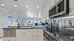 A modern kitchen with white cabinets, a black countertop, and a built-in microwave. - 604 Surf Villas Oceanfront Luxury Condo at Sawgrass Beach Club in Beautiful PVB! (Ponte Vedra Beach)