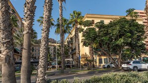 Una calle bordeada de palmeras y edificios, incluyendo un restaurante y un edificio de varios pisos con balcones.