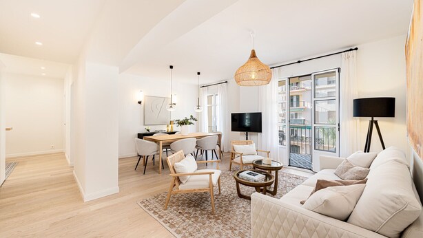 Un salón espacioso con un sofá grande, una zona de comedor con mesa y sillas, un televisor y un balcón con vistas.
