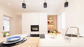 Una cocina moderna con armarios blancos, horno empotrado, lavamanos con grifo e iluminación colgante.