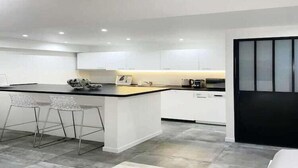 A modern kitchen with a central island, bar stools, and white cabinetry.