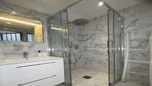 A modern bathroom with a glass-enclosed shower, marble walls, and a white vanity.
