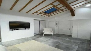 A spacious room with a high ceiling, a mounted TV, a white chair, and a wardrobe.