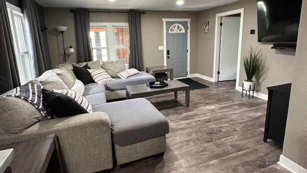 Een moderne woonkamer met een hoekbank, een salontafel en een flatscreen televisie aan de wand.