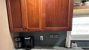 Een keuken met houten kastjes, een marmeren aanrecht, een koffiezetapparaat, en een bordje met de tekst 'DRINK COFFEE then get shit done'.