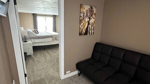 Een slaapkamer met een bed, een zwarte bank en een schilderij aan de muur.