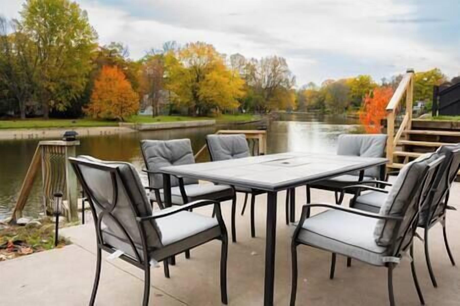 Une terrasse extérieure avec une table et des chaises, donnant sur un plan d’eau et les couleurs automnales du feuillage.