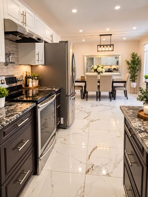 A modern kitchen with a built-in oven, stainless steel refrigerator, and marble flooring.