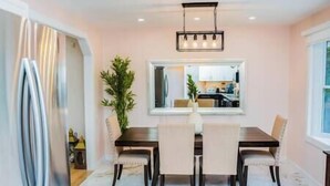 Un comedor con una mesa rectangular, cuatro sillas, una lámpara colgante y un ventanal grande.