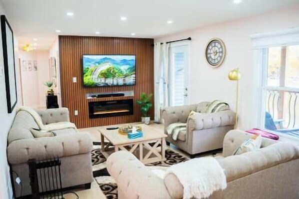 A living room with two sofas, a coffee table, a flat-screen TV mounted on a wooden panel wall, and a clock on the wall.