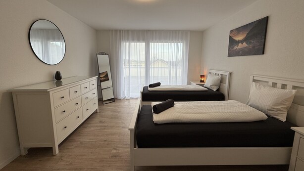 Une chambre avec deux lits, une commode, un miroir et une fenêtre avec des rideaux.