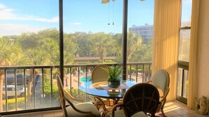 A balcony with a glass table, wicker chairs, and a potted plant. - Two bedroom condo on Siesta Key with 2 pools, marina, tennis courts & more! (Siesta Key)