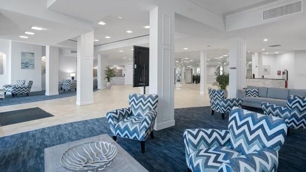 A modern lobby with zigzag patterned chairs, a grey sofa, and a reception desk. - Two bedroom condo on Siesta Key with 2 pools, marina, tennis courts & more! (Siesta Key)