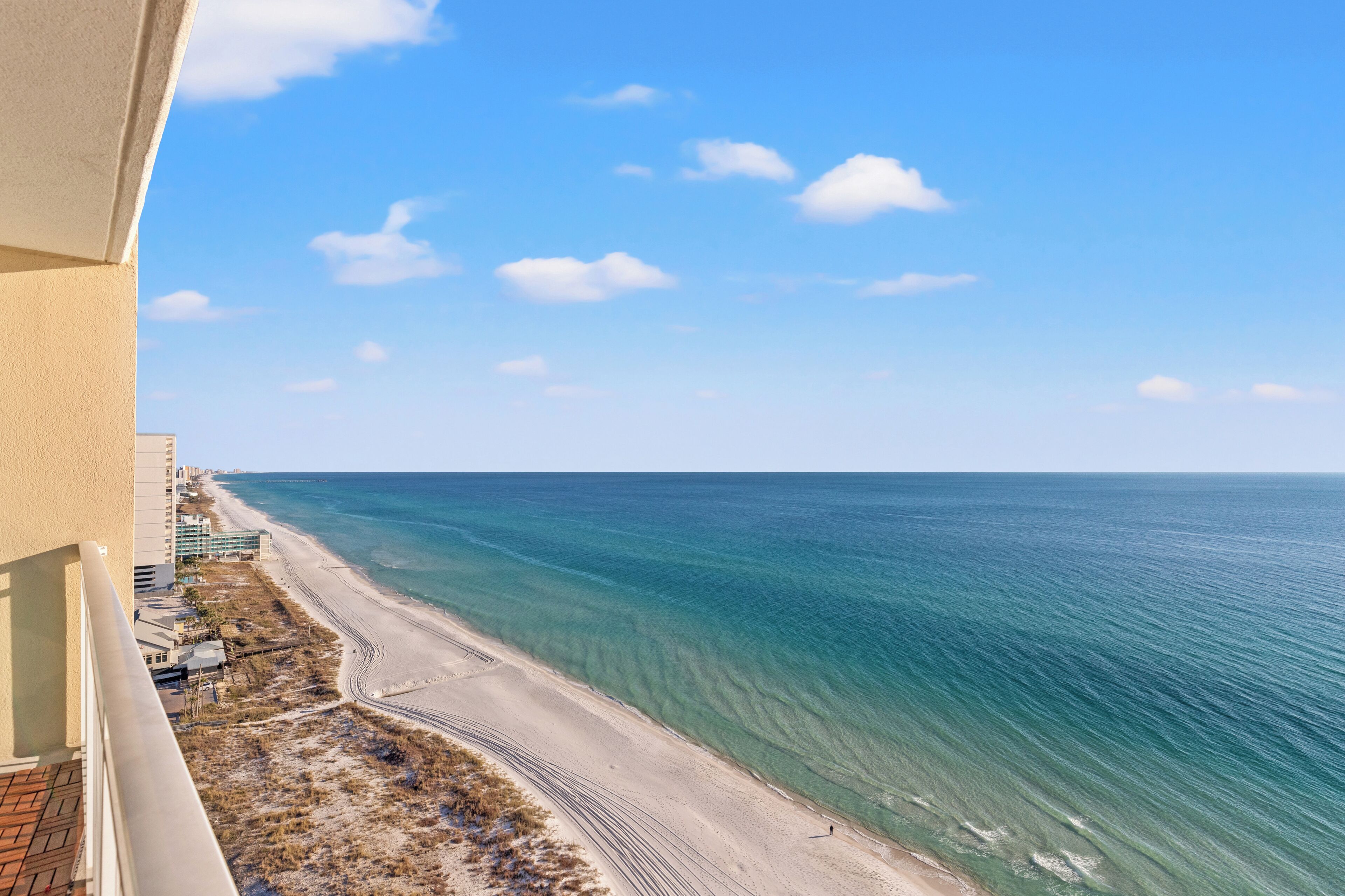 A beach view from a balcony overlooking a sandy beach and the ocean.