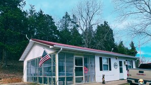 A small, single-story building with a red roof and large windows, surrounded by trees. - Springside Cottage in beautiful Eminence. Great outdoor space - NEW Hot tub! (Eminence)