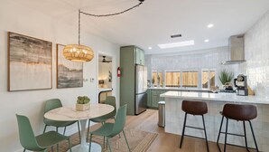 Uma cozinha moderna com ilha central, cadeiras verdes e luminária pendente.