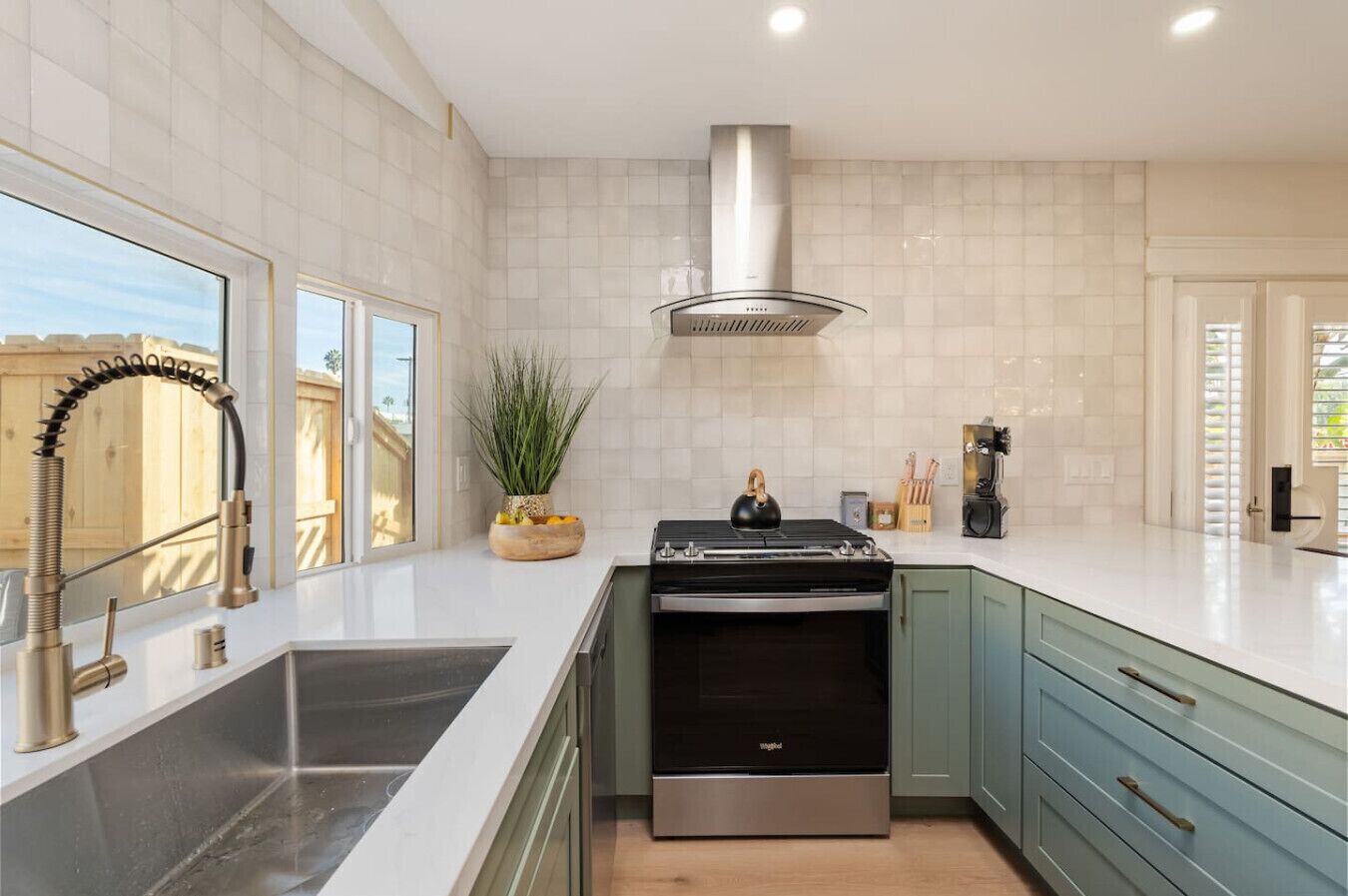 Uma cozinha moderna com uma pia de aço inoxidável, forno embutido e armários verde-claros.
