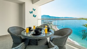 Een balkon met rieten meubels, een glazen tafel en uitzicht op zee en bergen.
