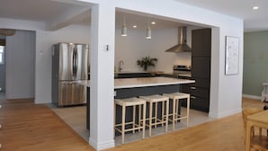 A modern kitchen with a stainless steel refrigerator, a gas stove, and pendant lights.