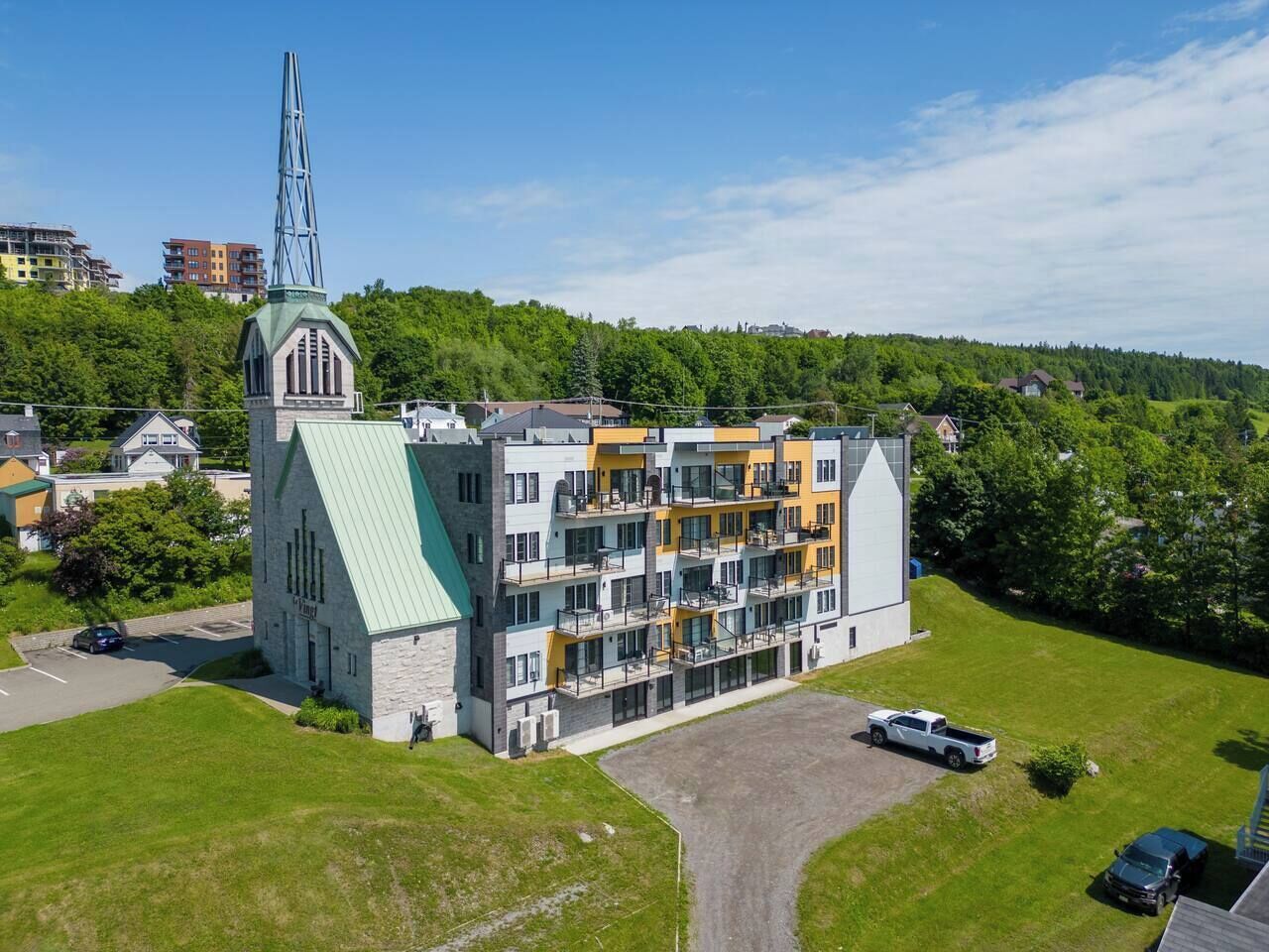 Un edificio de varios pisos con una destacada aguja de iglesia y un complejo moderno de apartamentos.