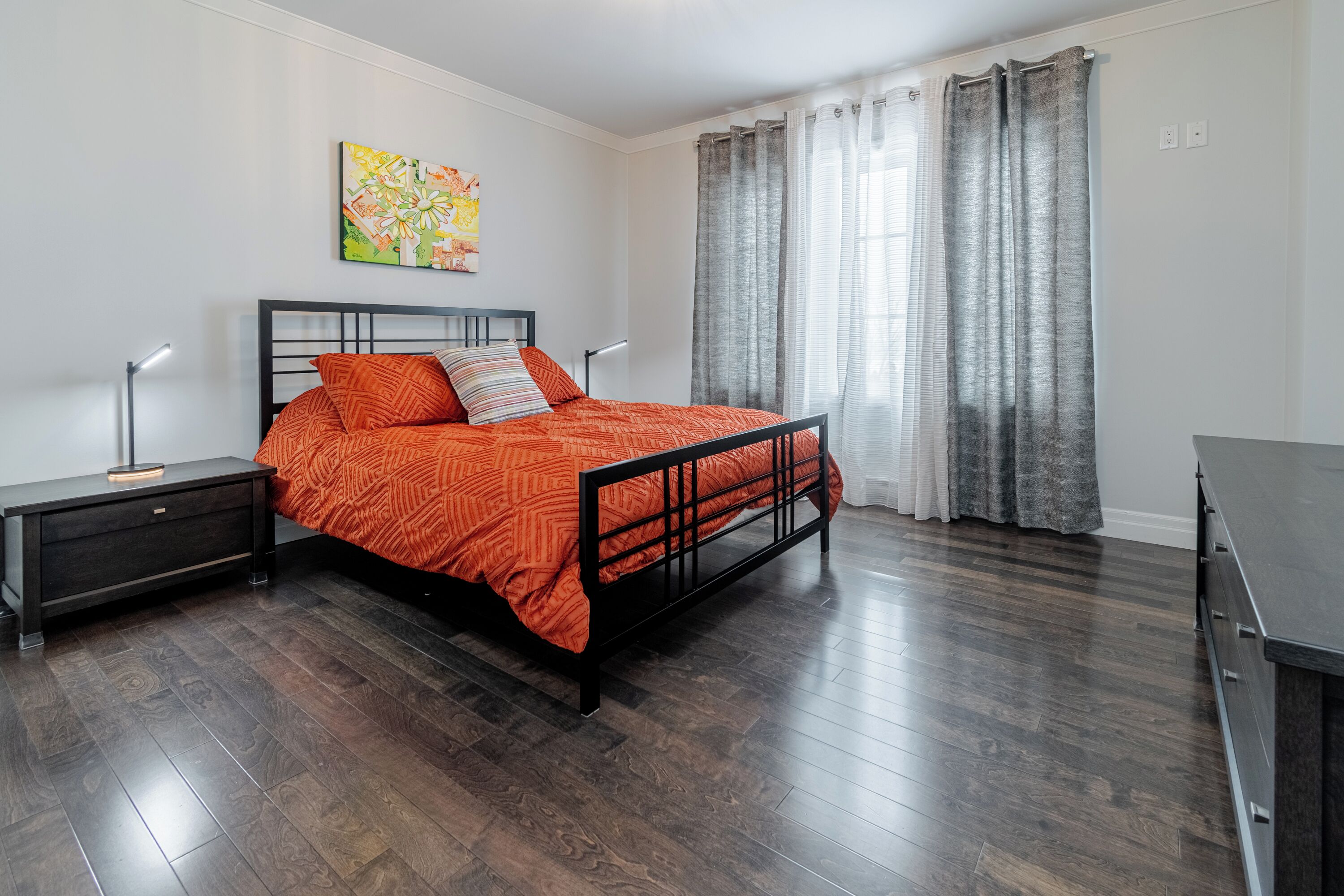 Une chambre à coucher avec un lit, des tables de chevet, un bureau et une fenêtre avec des rideaux.