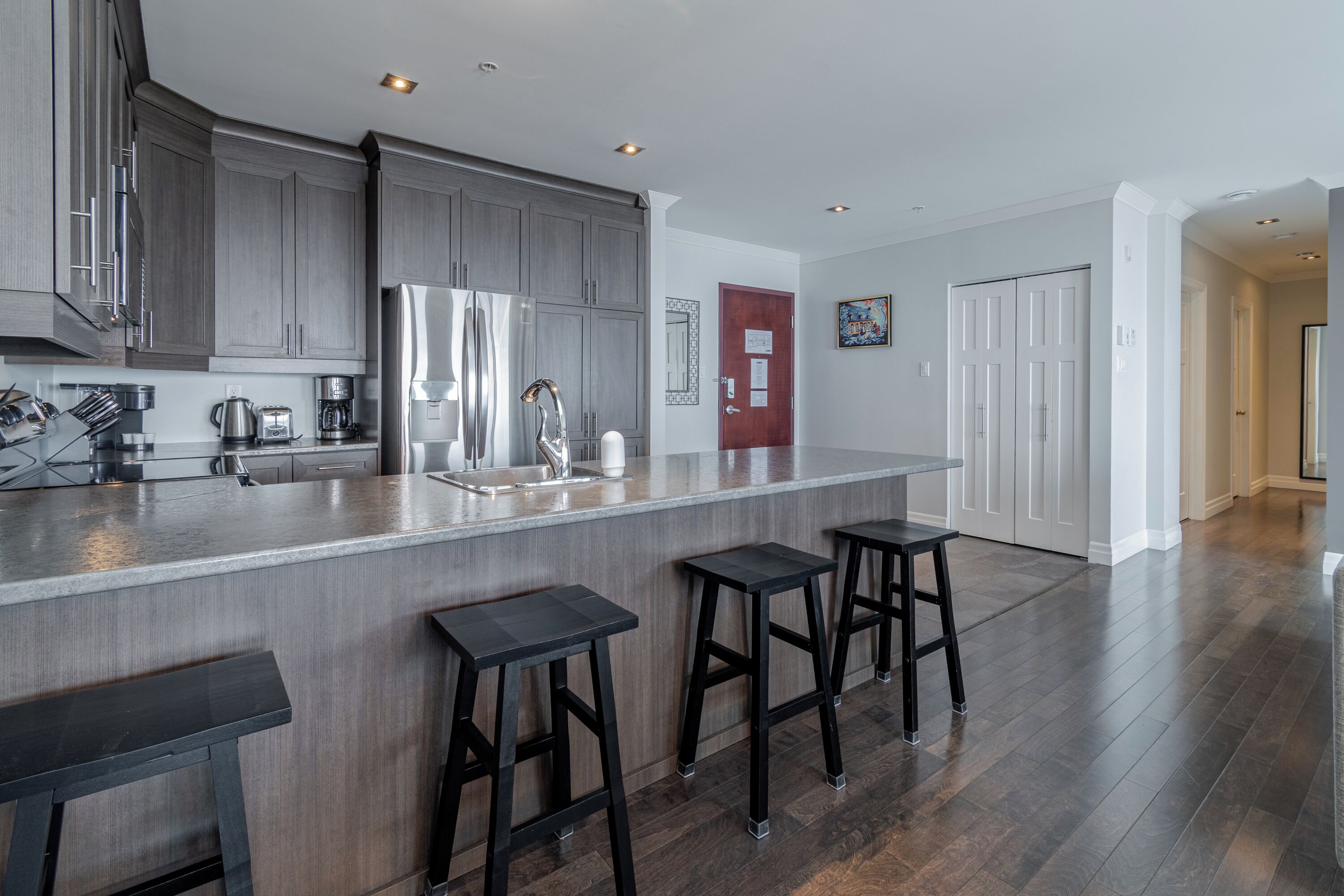 A modern kitchen with dark wood cabinets, stainless steel appliances, and a bar area with stools.