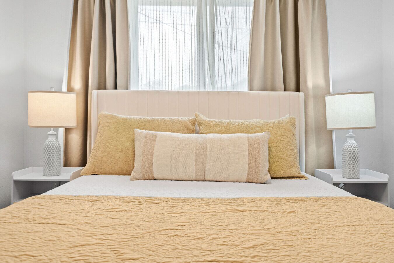 A bed with a textured beige blanket, two pillows, and a headboard. There are two bedside tables with lamps.