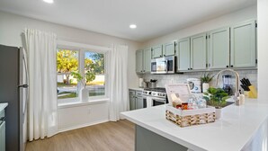 A modern kitchen with white cabinetry, a central island, and a window with curtains.
