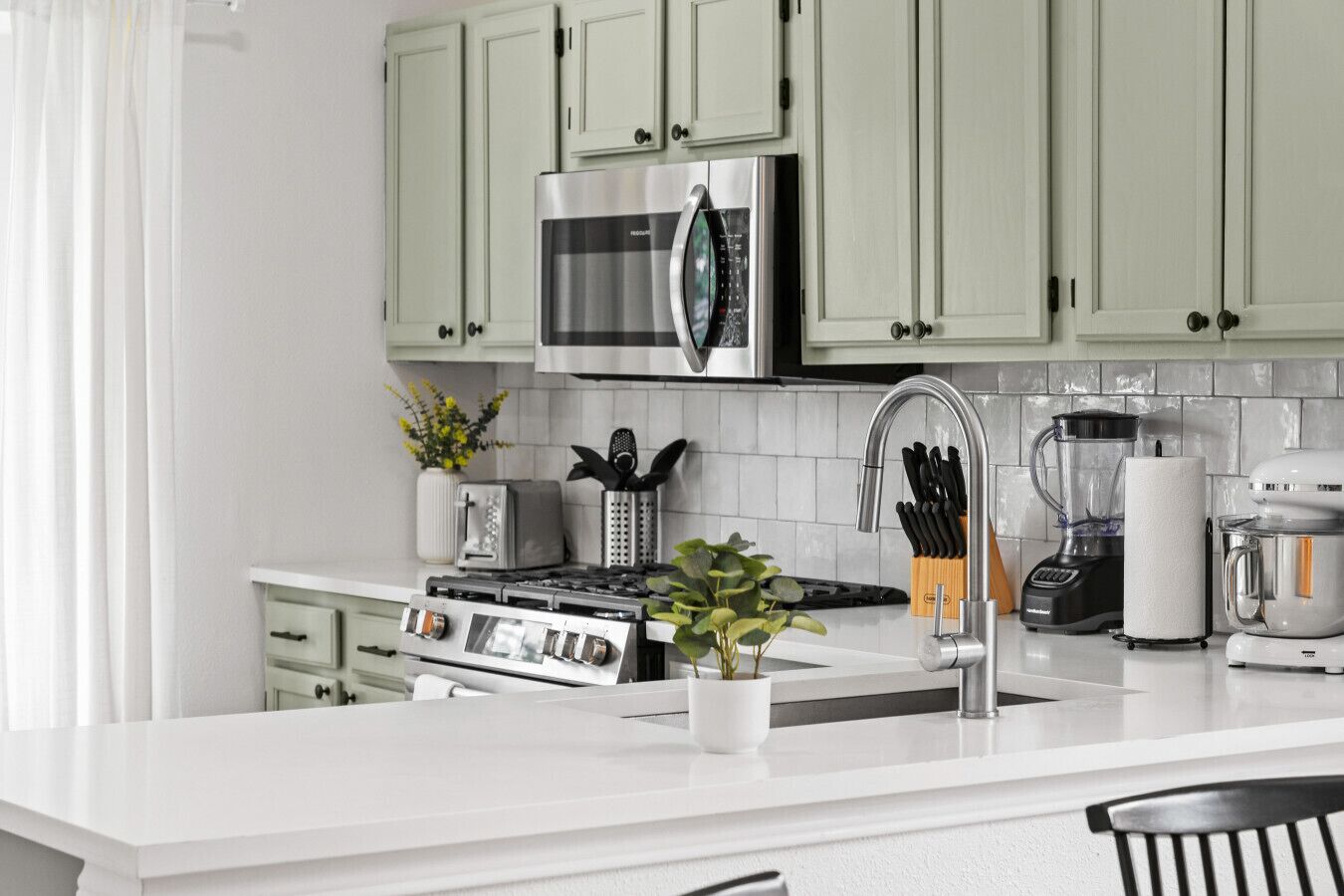 Une cuisine moderne avec des meubles de couleur vert clair, des appareils en acier inoxydable et un plan de travail blanc.