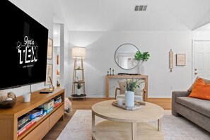 A modern living room with a flat-screen TV, wooden furniture, a round coffee table, and a fireplace.