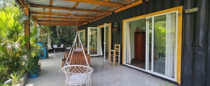 Un espace extérieur abrité, doté d’une table et de chaises en bois, d’un fauteuil suspendu et d’une grande porte-fenêtre coulissante.