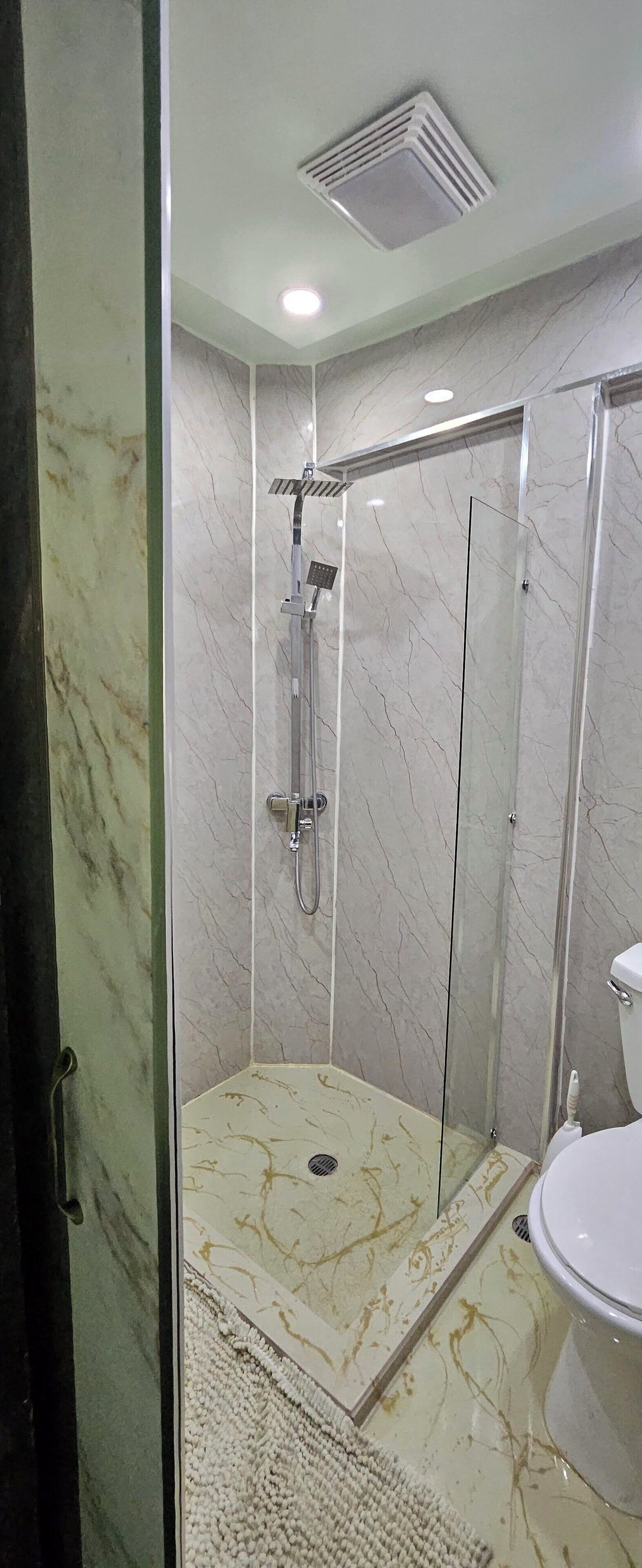 A modern bathroom with a glass-enclosed shower, a toilet, and marble flooring.