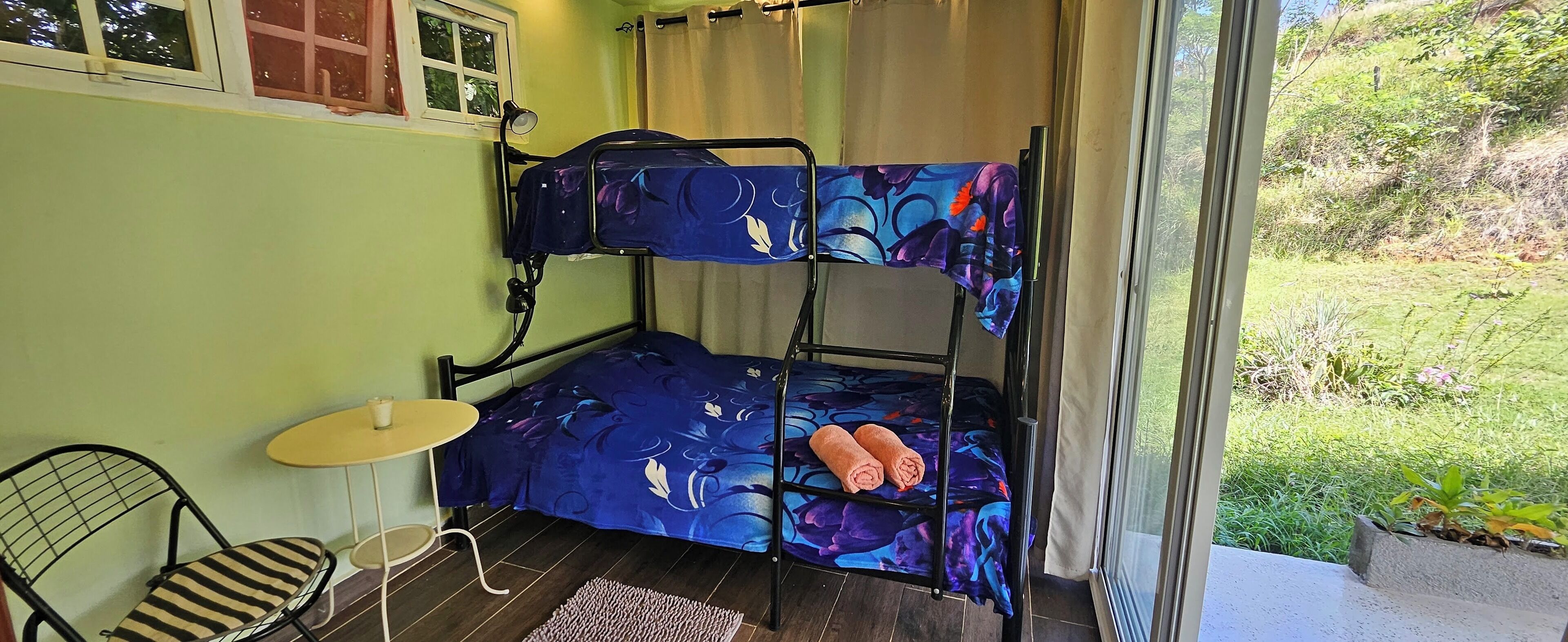 A bunk bed with floral bedding, a small table with a cup, and a chair.