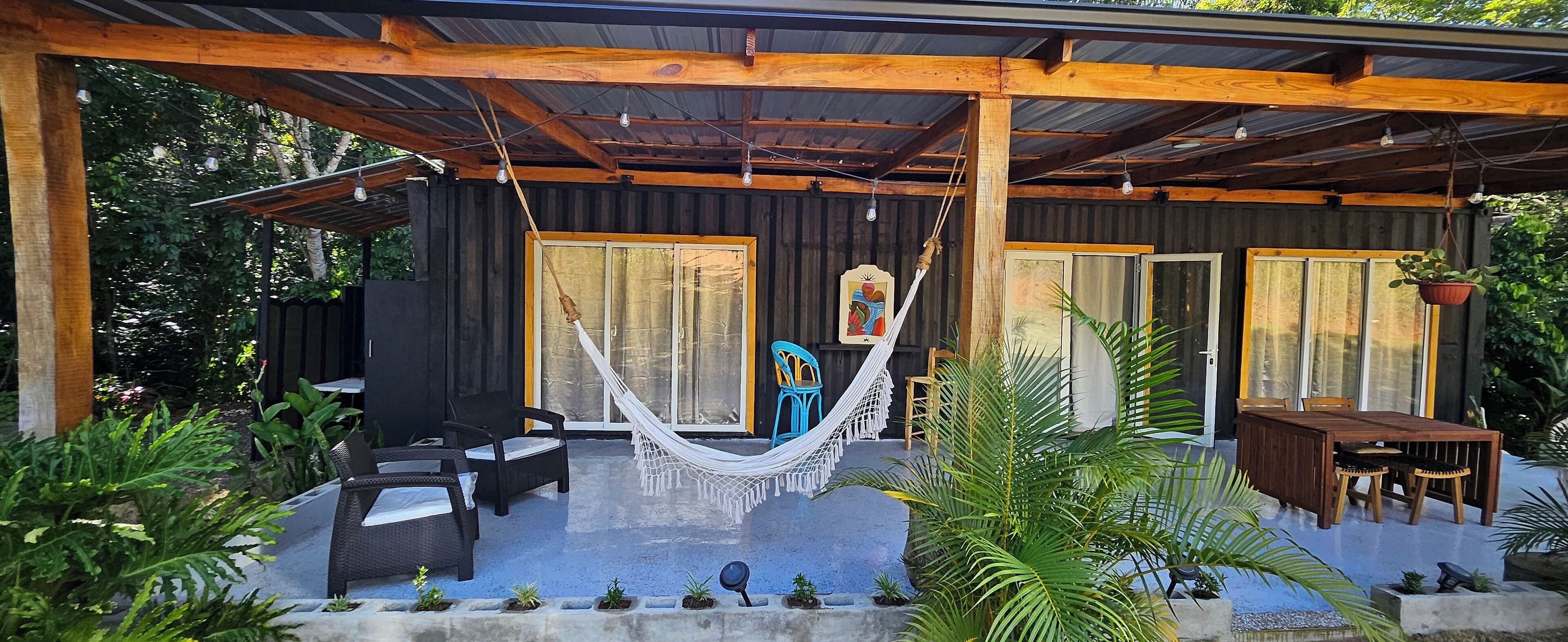 Un área de estar al aire libre con techo, que incluye una hamaca, sillas y una mesa.