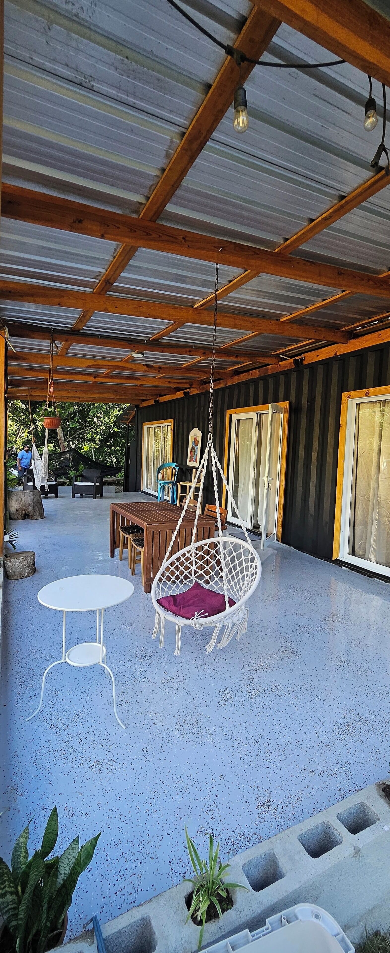 Un patio techado al aire libre con piso azul, muebles de madera, un sillón colgante y una mesa.