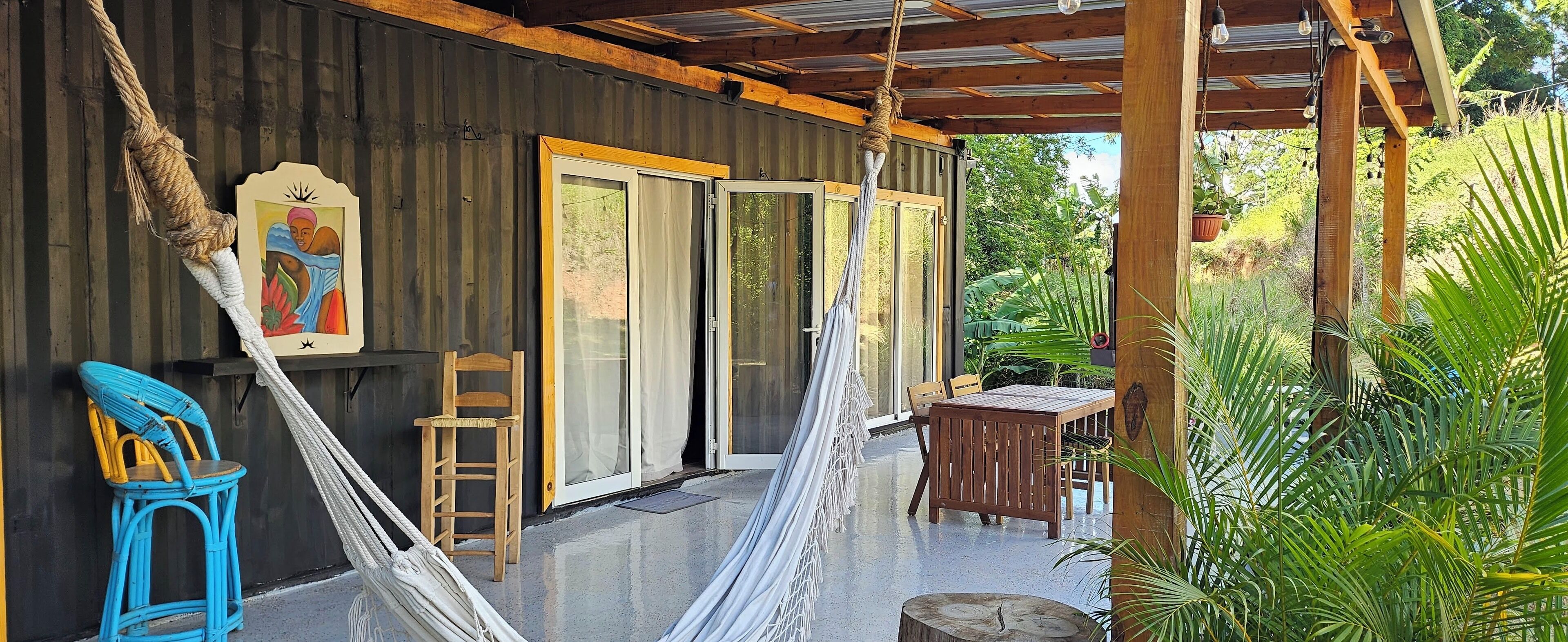 A covered outdoor area with a hammock, a wooden chair, a table, and a bench.