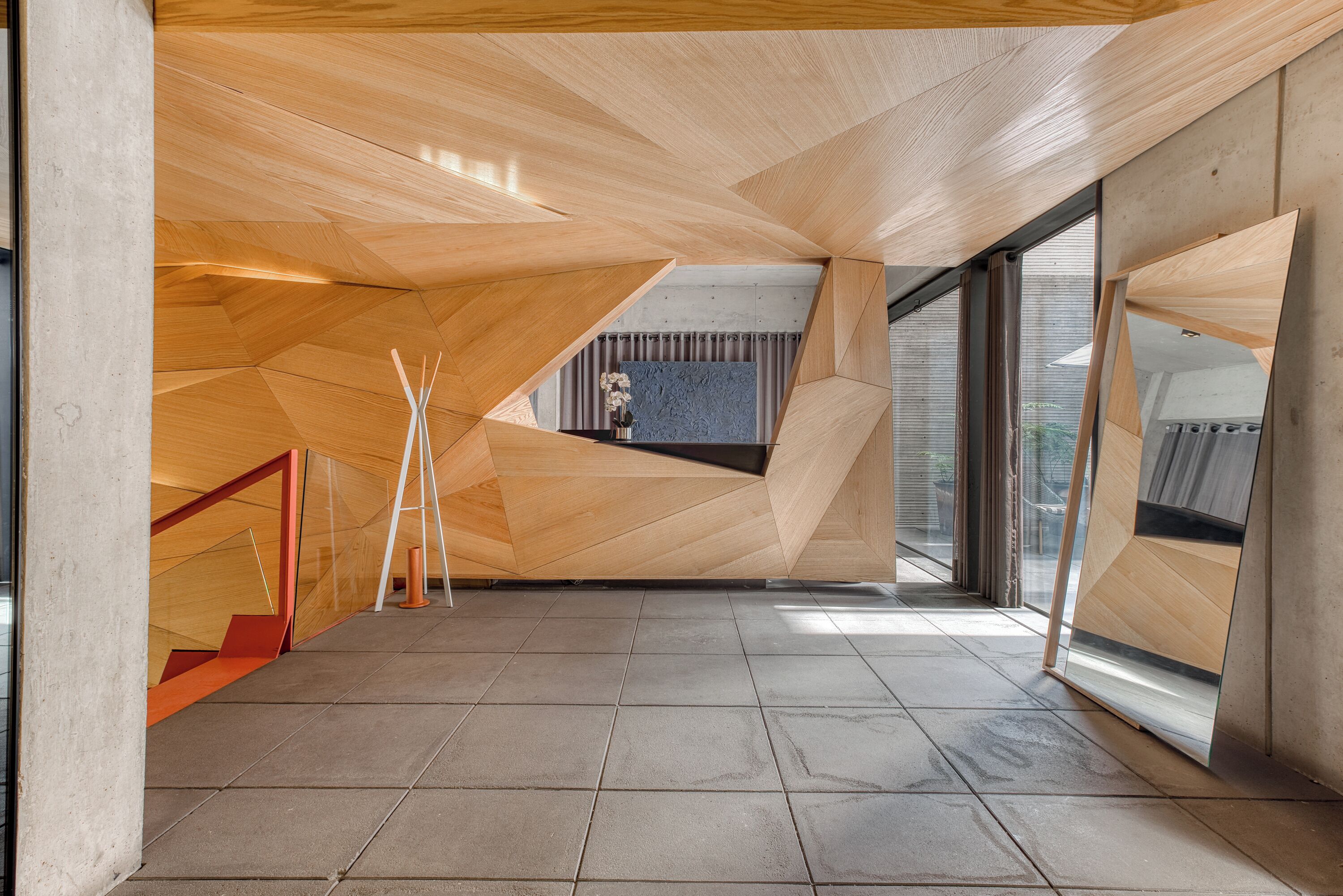 A spacious room with a geometric wooden ceiling, a tiled floor, and large windows allowing natural light.